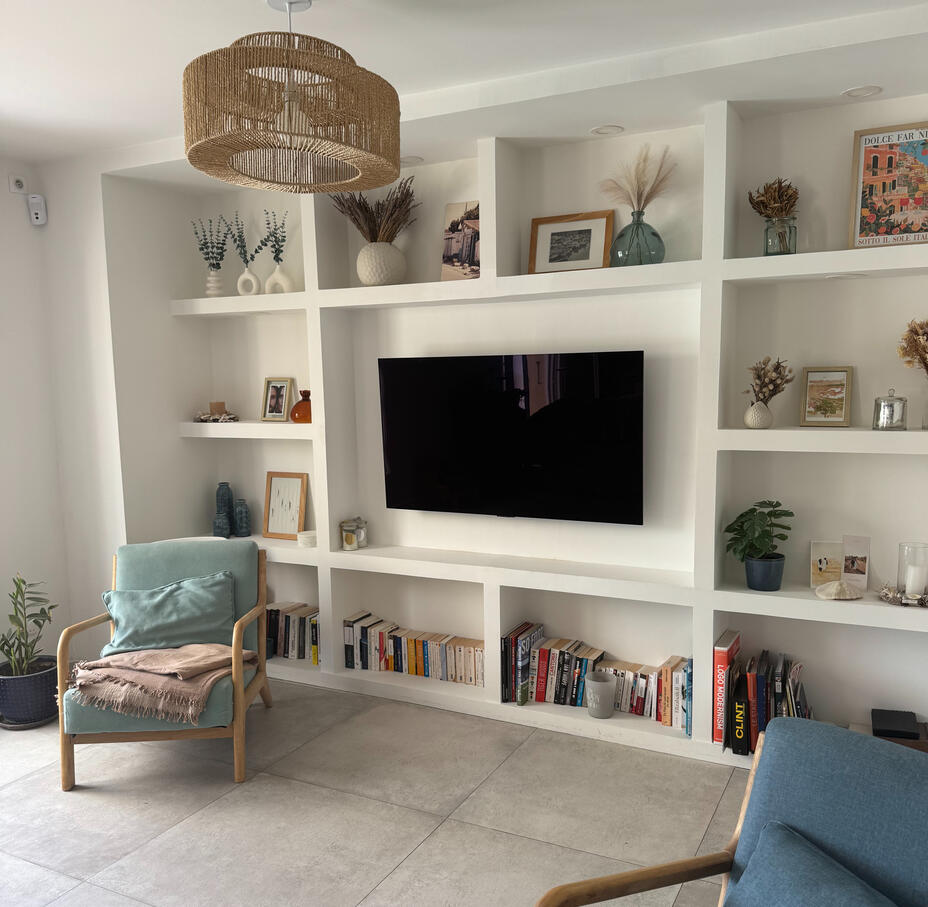 Salon avec rangements sur mesure — Atelier Luzons Salon avec bibliothèque murale blanche sur mesure intégrant la télévision, fauteuil bleu et plantes, agencement Atelier Luzons