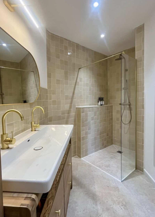 Salle de bain double vasque vue en plongée — Atelier Luzons Salle de bain avec douche à l'italienne, double vasque et robinetterie dorée vue de dessus, rénovation Atelier Luzons