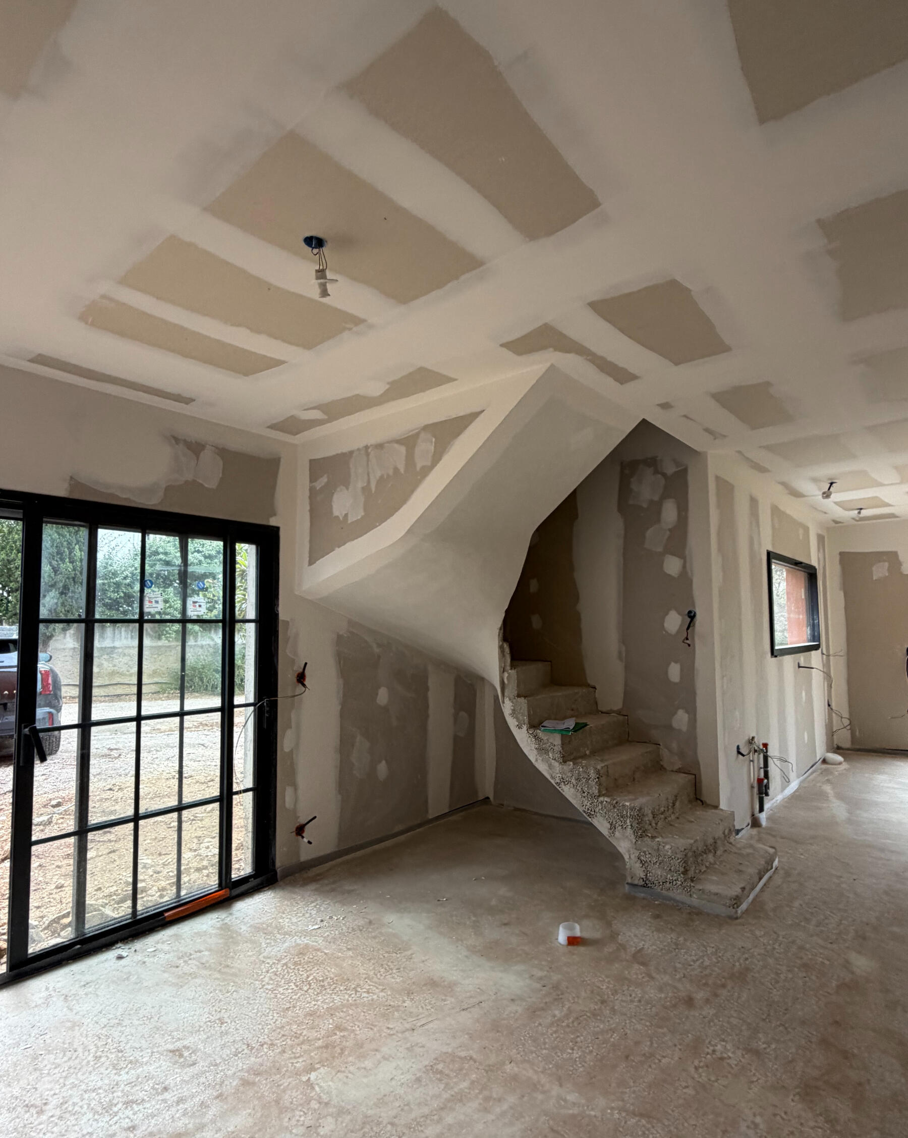 Rénovation en cours à Marseille par Atelier Luzons Salon en cours de rénovation avec escalier hélicoïdal et grande baie vitrée, chantier suivi par Atelier Luzons à Marseille